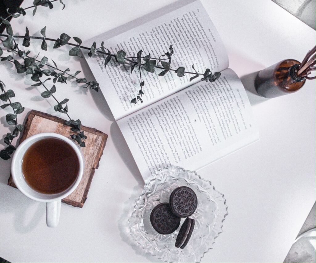 Tea and Oreos on a white table with a book open and plant. pamper yourself
