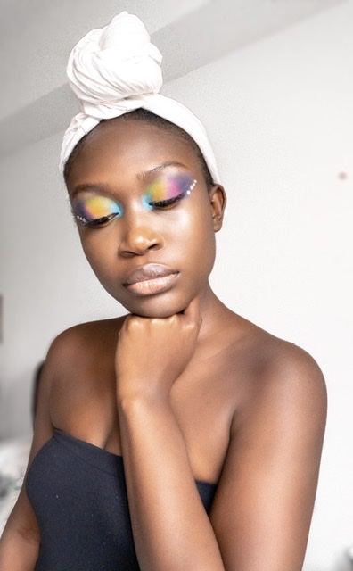 Dark skin back girl with fluffy brows and clear skin, applying colourful eyeshadow.