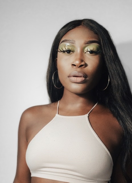 Darkskin black woman with long hair, showing how to achieve glossy green eyeshadow makeup.