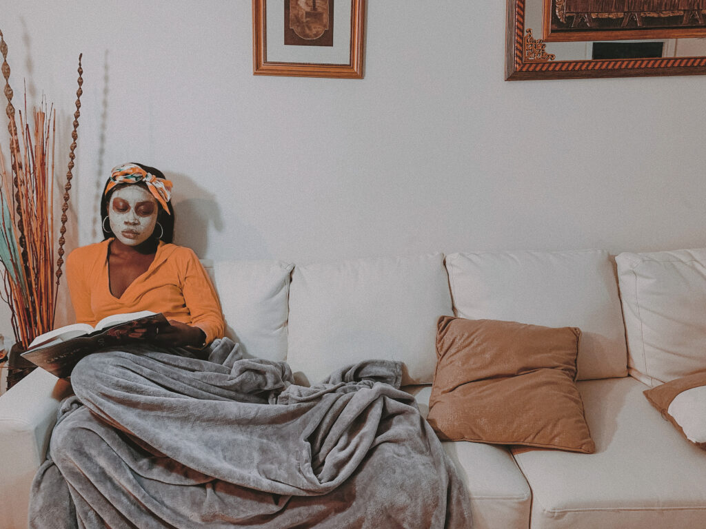 black woman in a cosy yellow sweater reading a book on the couch