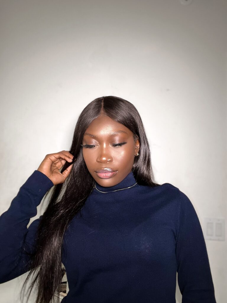 black woman in blue turtle neck and straight hair with soft glam makeup on.